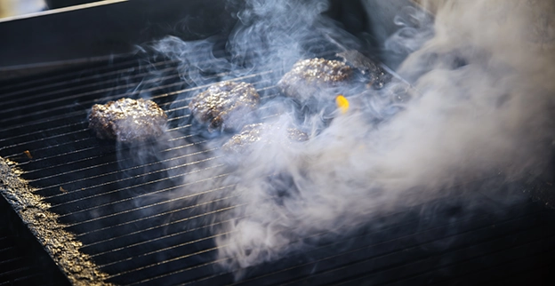 Burger patties cooking on a grill with smoke rising.