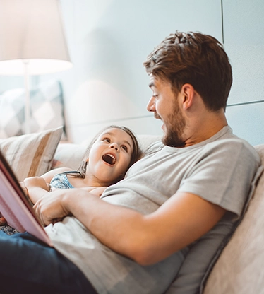 A father and daughter laughing in the couch.