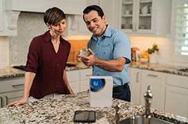 AireServ tech showing thermostat to customer in kitchen.