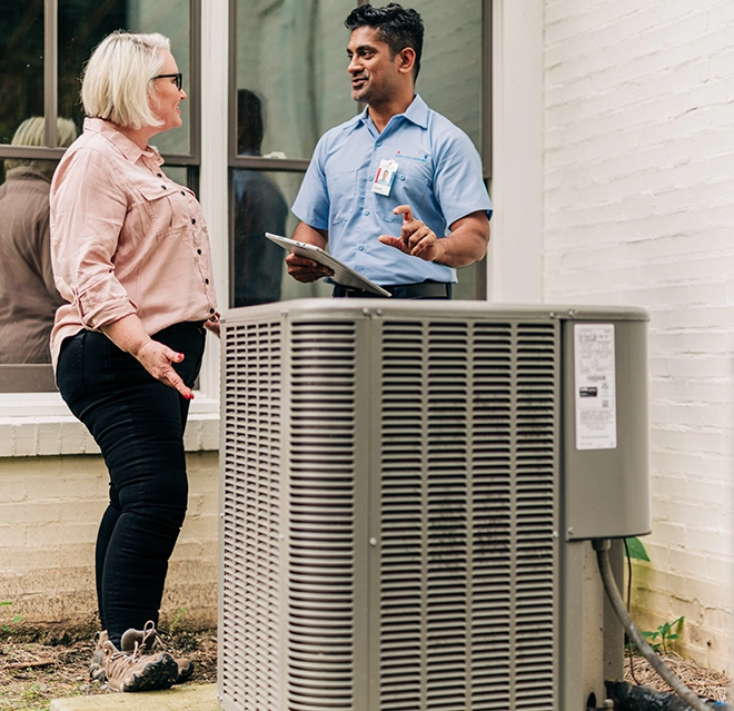 An Aire Serv technician talking to a customer next to an air conditioning unit.