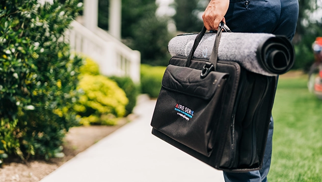 Aire Serv professional walking up to a customers home with an Aire Serv bag in hand.