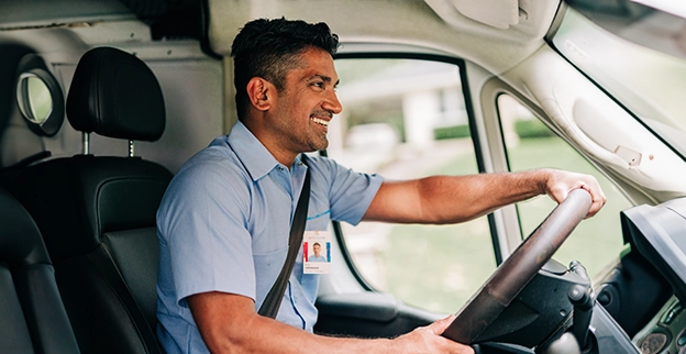 Smiling Aire Serv service professional driving van outside customer building.